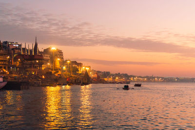 Illuminated buildings by sea against sky during sunset