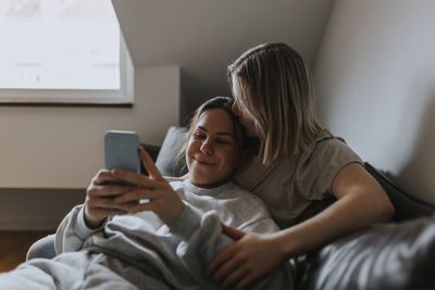 Female couple relaxing together on sofa and looking at cell phone