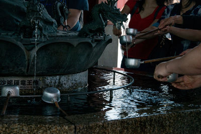 Midsection of people holding bamboo dippers by pond