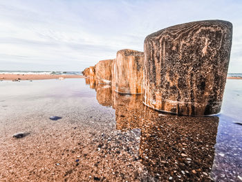 Wood formation on beach against sky