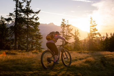  woman riding her mountain bike in early morning light on footpath, lens flare, backlight, in austria