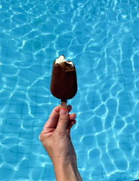 Close-up of hand holding chocolate ice cream against swimming pool.