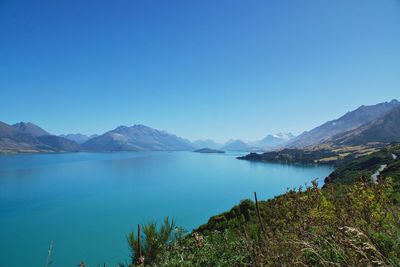 Scenic view of lake and mountains against clear blue sky