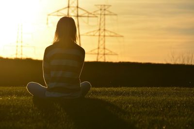 Rear view of woman sitting on grassy field during sunset