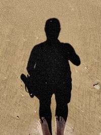 Low section of man standing with shadow on shore at beach
