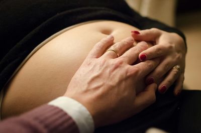 Cropped hand of husband touching pregnant wife belly at home