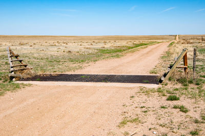 Dirt road amidst field against sky