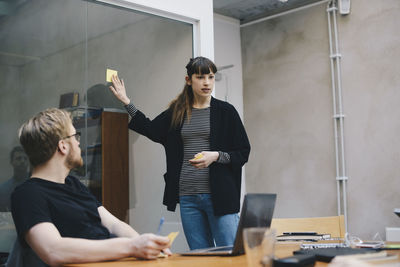 Female computer programmer showing adhesive note while giving presentation to colleague in office