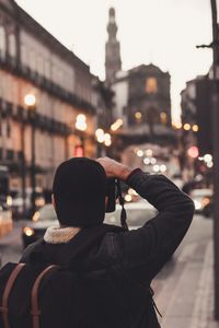 Rear view of man photographing on illuminated street in city