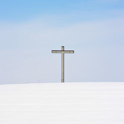 Cross on snow covered landscape against sky