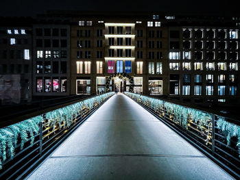 Illuminated footpath amidst buildings in hamburg city at night
