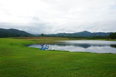 Scenic view of field by lake against sky