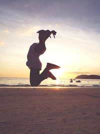 Man jumping at beach against sky during sunset