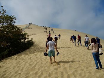 Rear view of people walking on sand against sky