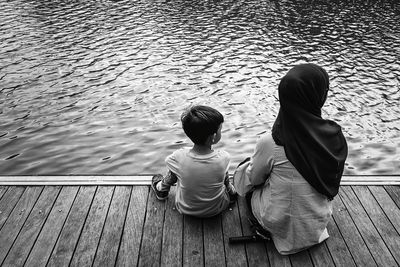 Rear view of mother and son sitting on pier over lake