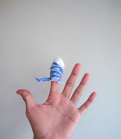 Cropped hand of person with index finger wound dressed against light background 