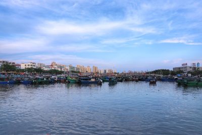 Boats in river by buildings against sky