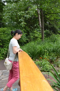 Side view of woman standing by railing against trees