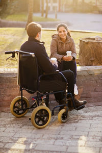 Young woman and man on wheelchair having coffee break