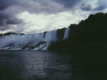 Scenic view of waterfall against cloudy sky