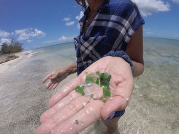 Midsection of woman showing stones at beach against sky