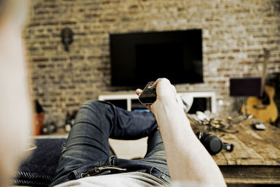 Man lying on the couch using remote control, partial view