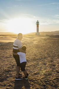 Full length of grandfather with grandson standing on land against lighthouse