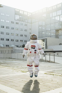 Female astronaut in mid-air near building during sunny day