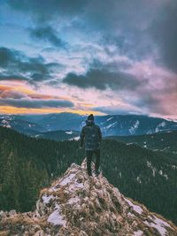 Rear view of man standing on mountain against cloudy sky