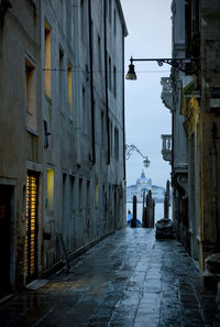 Wet footpath amidst buildings leading towards canal