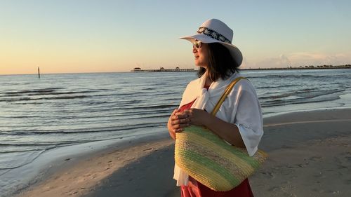 Woman standing on beach against sky at sunset