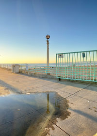 Street light on footpath by sea against clear blue sky