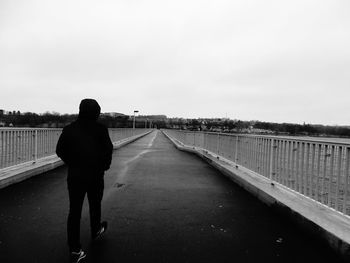 Rear view of man walking on bridge over river against sky