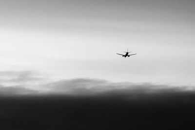 Low angle view of silhouette airplane flying against cloudy sky