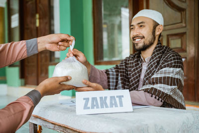 Smiling young man giving bag of rice in mosque