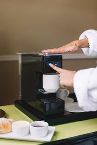 Unrecognizable caucasian woman put capsule into coffee machine. next to it is a croissant with jam