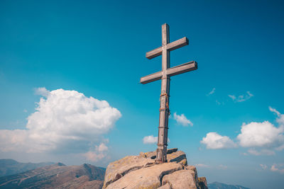 Low angle view of cross on rock against sky