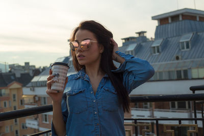 Young woman holding disposable cup while standing on building terrace