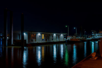 Illuminated buildings by sea against sky at night