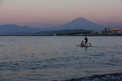 Man surfing in sea against sky during sunset