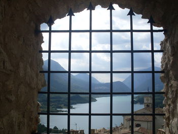 Lake barrea and mountains against sky seen from metal grate window