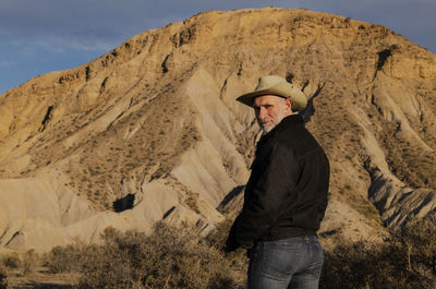 Adult man in cowboy hat standing against mountains in tabernas desert. almeria, spain