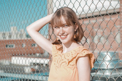 Portrait of smiling woman standing by chainlink fence