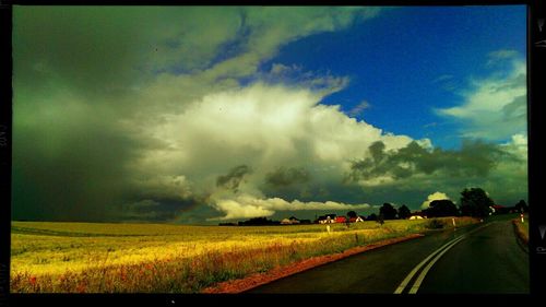 Road passing through field against cloudy sky