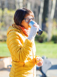 Happy wide smiling women in bright yellow jacket is holding thermos mug. hot tea or other beverage.