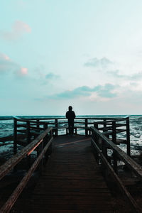 Man standing on pier while looking at sea against sky