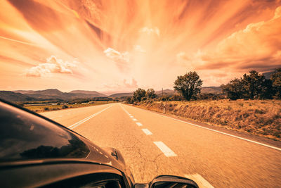 Road amidst field against sky during sunset