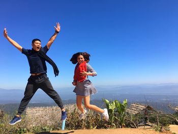 Full length of woman with arms raised against clear blue sky