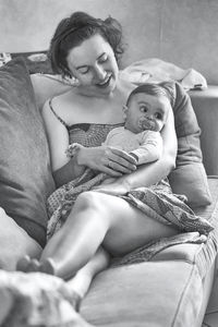 Smiling mother carrying toddler while sitting on sofa at home