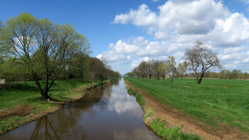 Footpath by river against cloudy sky